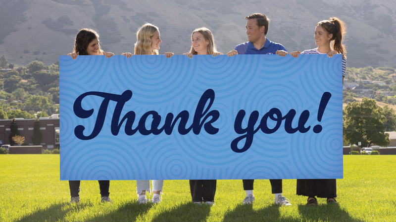 Five BYU students holding a large sign that reads "Thank You"