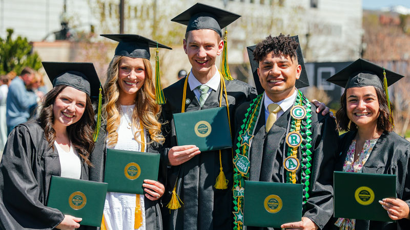 Five Ensign College graduates holding up their diplomas